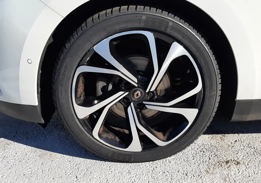 Gros plan sur la roue avant gauche blanche nacrée du Renault Scénic IV avec jante noire et argentée au design moderne.