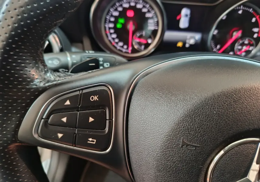 Gros plan sur le volant cuir noir de la Mercedes GLA 200 d, avec commandes multifonctions et tableau de bord en arrière-plan.