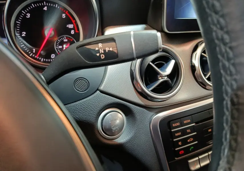 Vue rapprochée de la console centrale et du levier de vitesses d'une Mercedes GLA 200 d gris clair, avec bouton démarrage et aérateurs ronds.