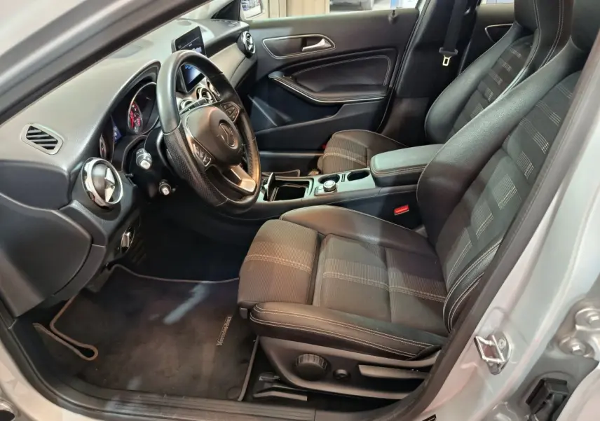 Intérieur avant droit de la Mercedes GLA 200 d gris clair, sièges noirs, volant cuir et console centrale avec molette.