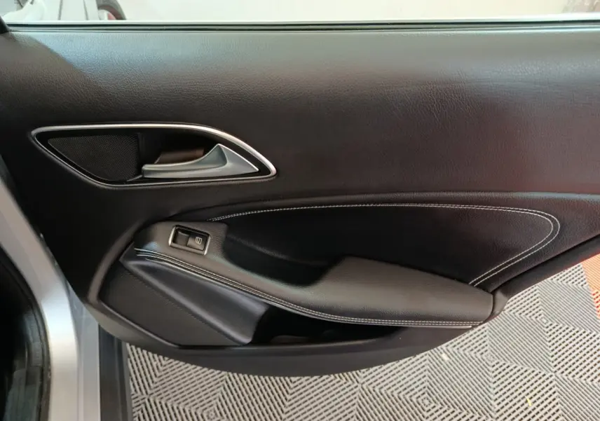 Gros plan sur la porte intérieure côté gauche d'une Mercedes GLA 200 d Business Executive gris clair, avec garniture cuir noire et surpiqûres blanches.