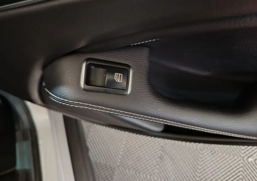 Gros plan sur la commande de lève-vitre en cuir noir avec surpiqûres blanches, porte côté conducteur d'une Mercedes GLA gris clair.