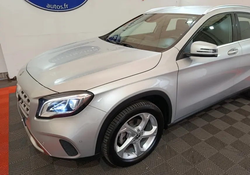 Mercedes GLA 200 d gris clair vu en 3/4 avant droit, avec phares LED allumés et jantes alliage visibles.