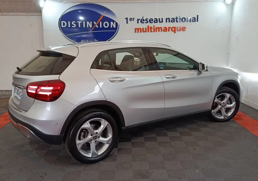 Vue de profil côté droit d'un Mercedes GLA 200 d Business Executive gris clair avec feux arrière allumés en intérieur showroom.
