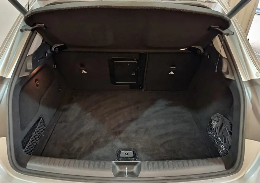Coffre ouvert vu de l'arrière d'un Mercedes GLA 200 d gris clair, avec tapis noir et filet de rangement latéral.