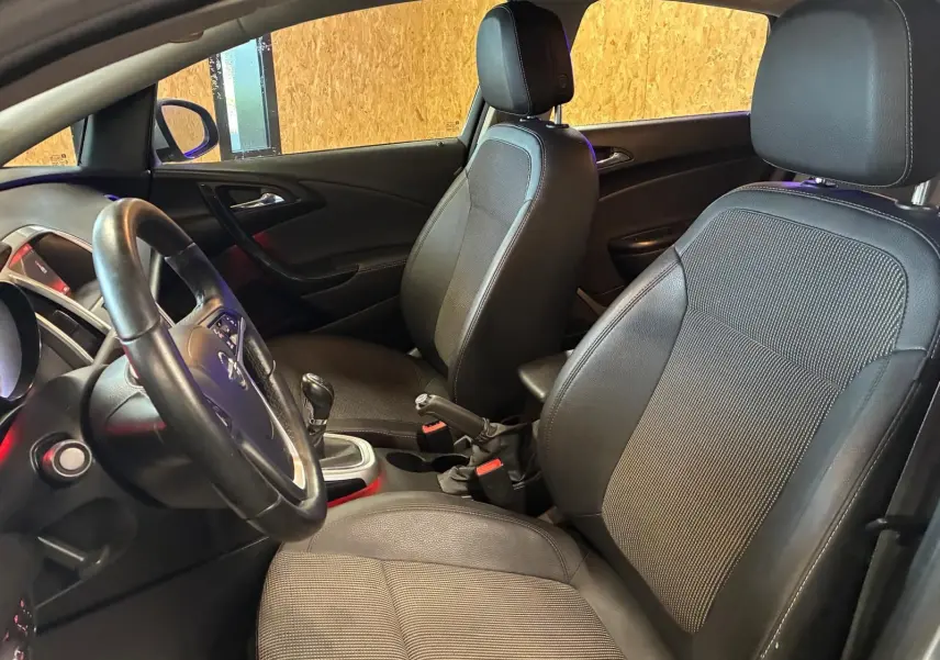 Intérieur avant de l'Opel Astra 1.6 CDTI 2015, vue côté conducteur, sièges noirs en tissu et cuir, levier de vitesse manuel visible.