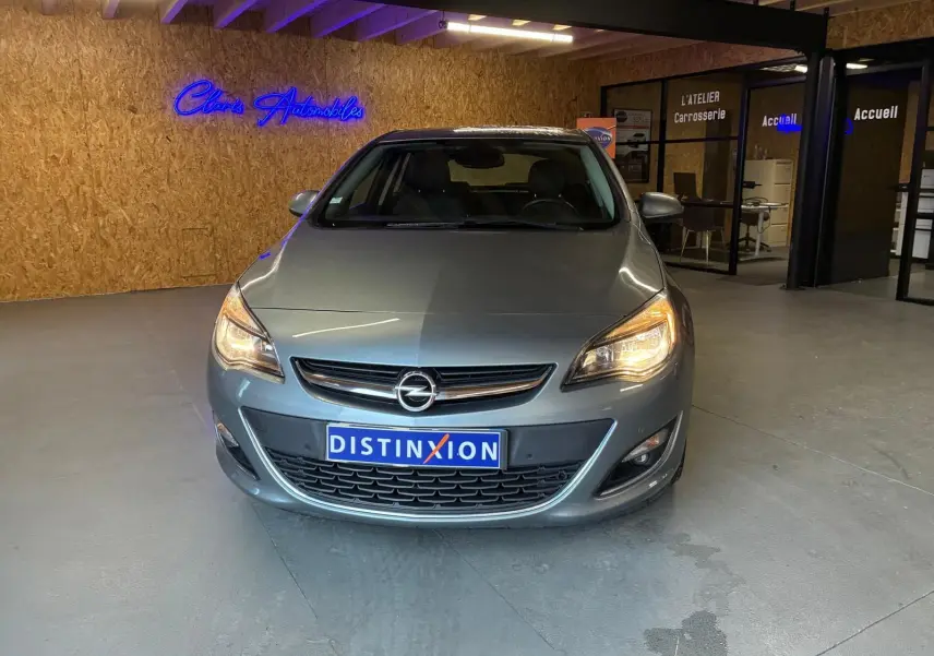 Vue avant d'une Opel Astra gris métallisé 2015 avec phares allumés dans un showroom intérieur.