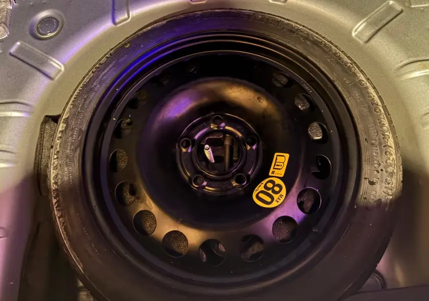 Gros plan sur la roue de secours noire avec étiquette jaune 80 km/h dans le coffre d'une Opel Astra gris 2015.