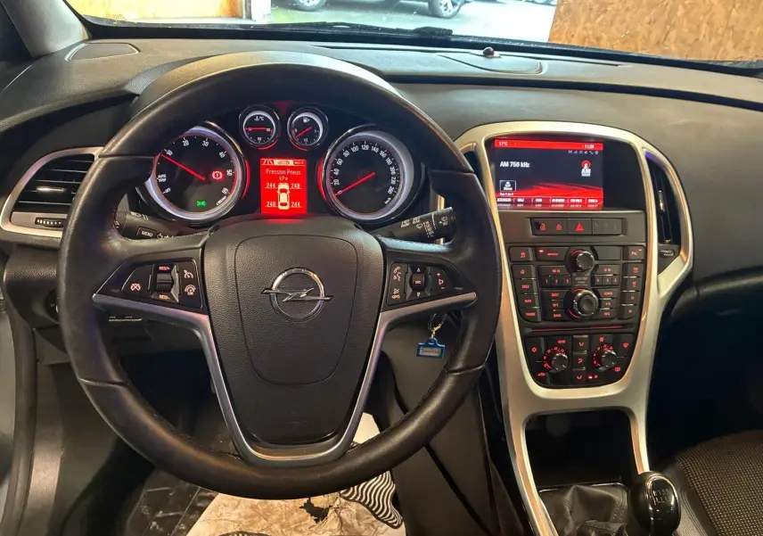 Vue intérieure centrée sur le volant et le tableau de bord de l'Opel Astra gris, avec écran central et levier de vitesse manuel.