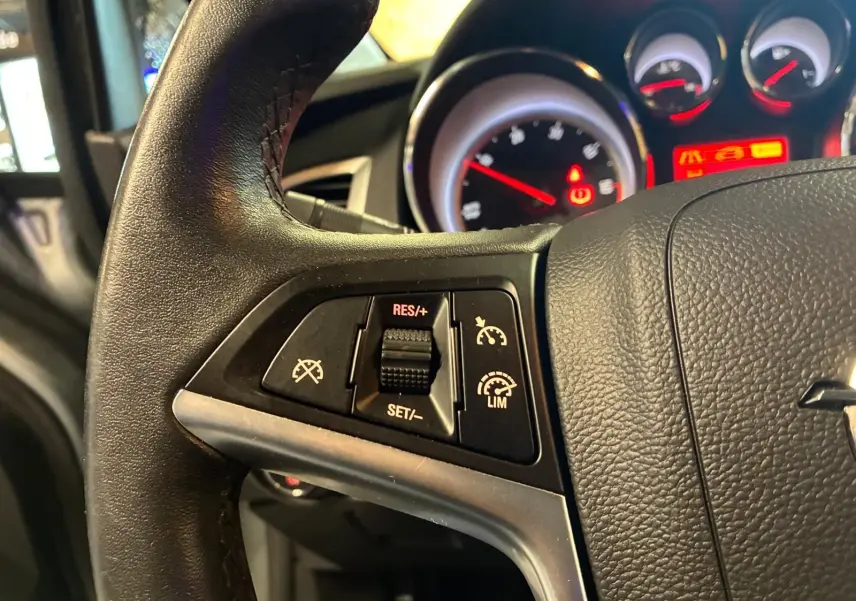 Gros plan sur le volant noir de l’Opel Astra 2015 avec commandes de régulateur de vitesse et tableau de bord éclairé.
