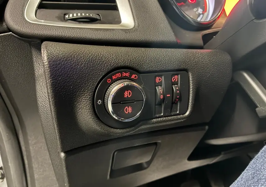 Gros plan sur le tableau de bord côté gauche de l'Opel Astra gris, montrant les commandes d'éclairage avec voyants rouges.