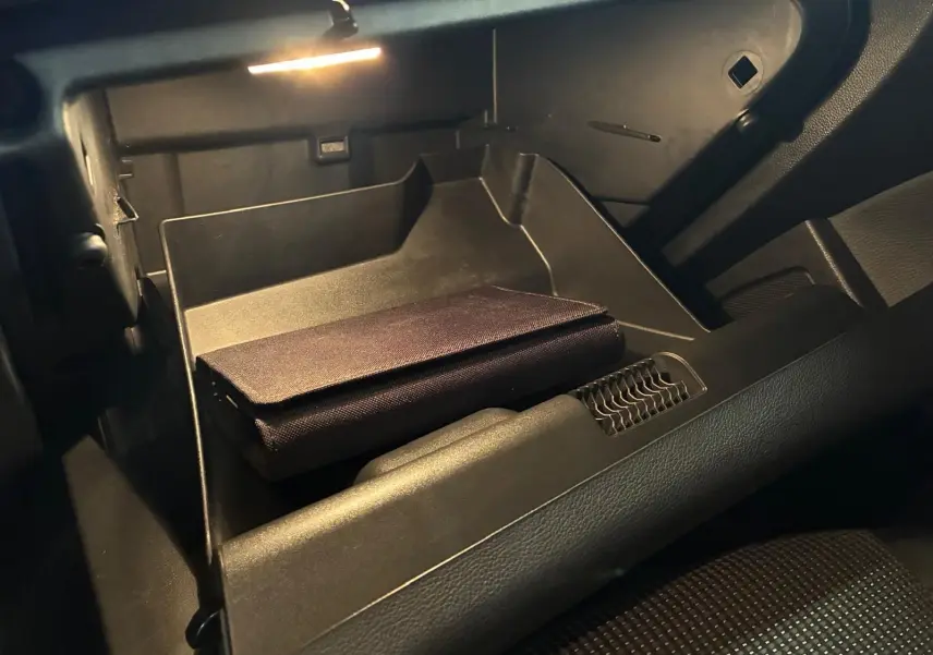 Vue intérieure du vide-poche passager éclairé d'une Opel Astra gris 2015, avec un étui noir posé à l'intérieur.