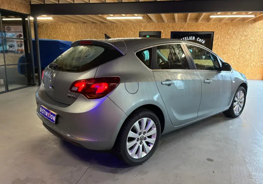 Opel Astra gris vue 3/4 arrière droit dans un garage avec feux arrière allumés et jantes alliage.