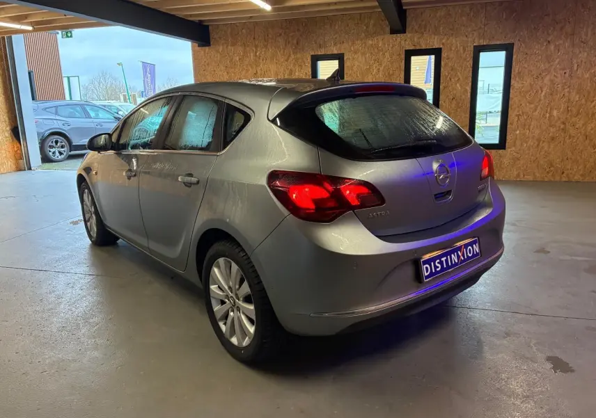 Opel Astra gris 2015 vue 3/4 arrière droit dans un garage, feux arrière allumés et plaque Distinxion visible.