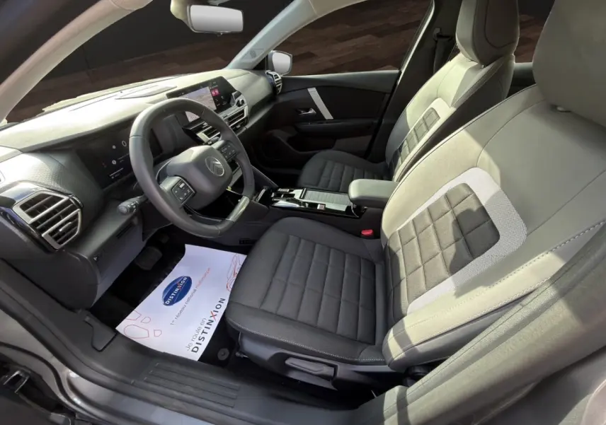 Vue intérieure côté conducteur de la Citroën C4 hybride 2025, sièges gris à motifs carrés et tableau de bord moderne.