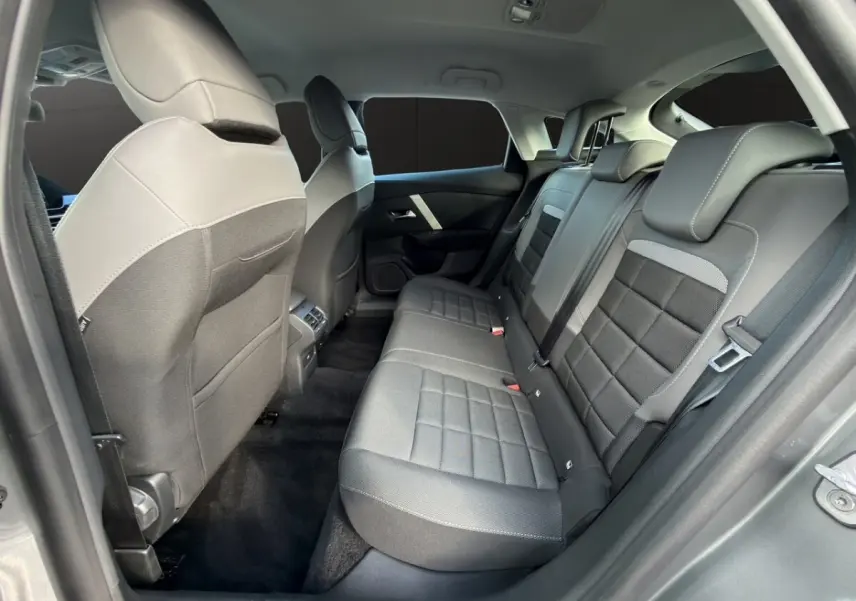 Vue intérieure arrière droite de la Citroën C4 hybride 2025, sièges tissu gris foncé avec appuie-têtes intégrés.