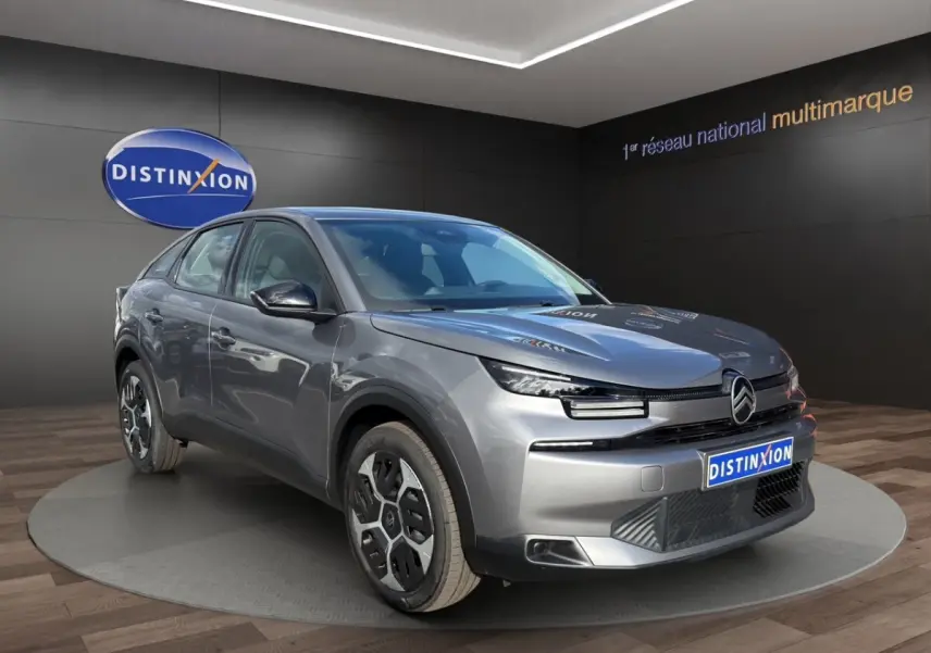 Citroën C4 hybride gris foncé vue 3/4 avant avec phares LED et jantes spécifiques en exposition showroom.