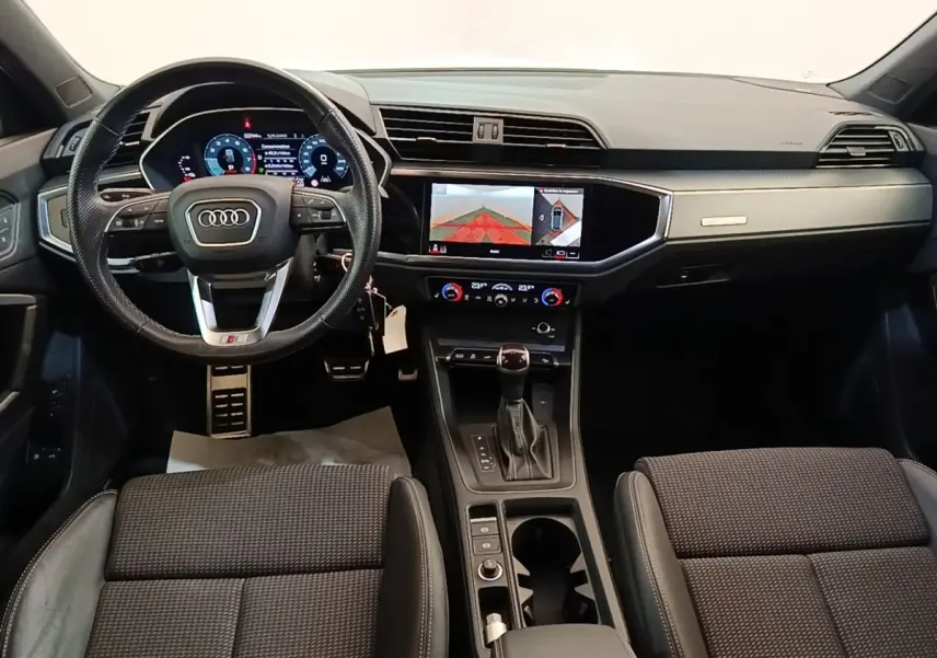 Vue intérieure avant de l'Audi Q3 Sportback 2024, tableau de bord noir avec écran tactile et volant multifonctions cuir.