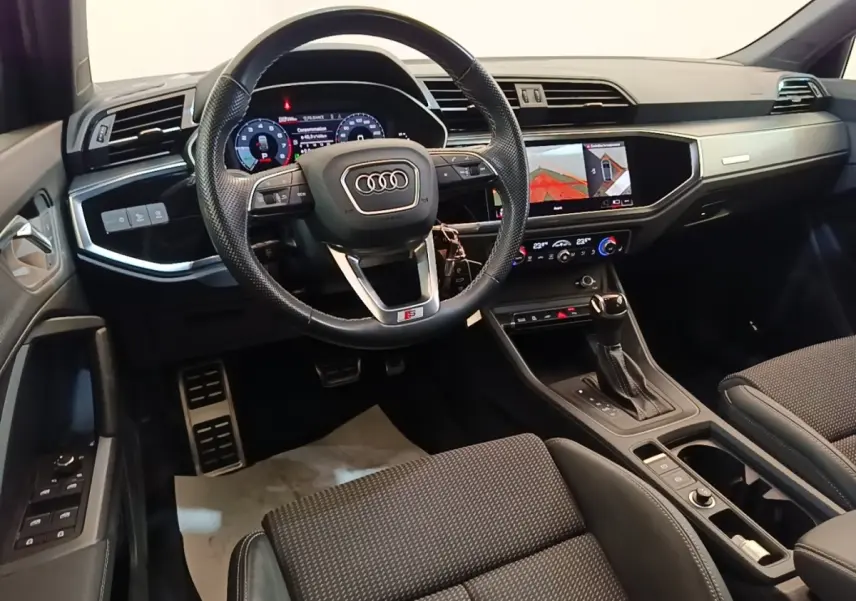Vue intérieure avant de l'Audi Q3 Sportback 2024, tableau de bord noir avec écran tactile et volant cuir multifonctions.