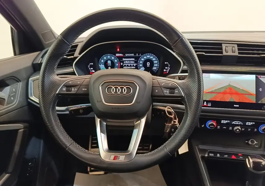 Vue intérieure centrée sur le volant cuir S Line et le tableau de bord digital de l'Audi Q3 Sportback gris clair 2024.