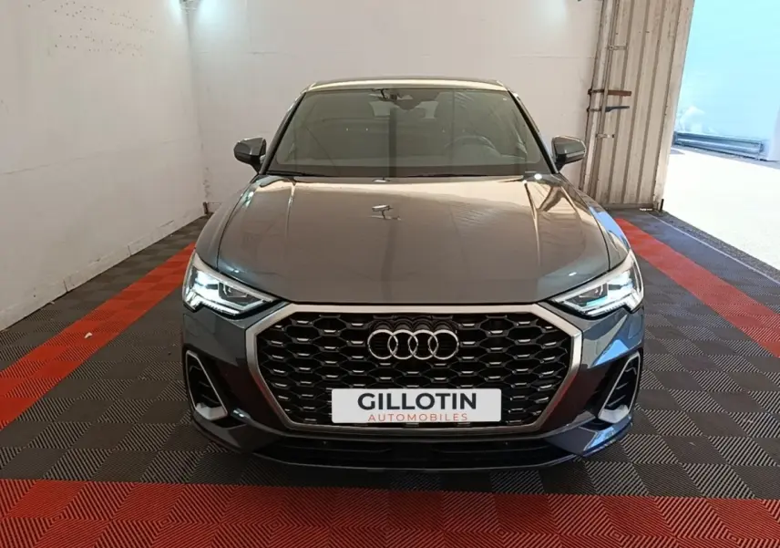 Vue avant d'un Audi Q3 Sportback gris clair avec calandre hexagonale et phares LED allumés dans un garage.