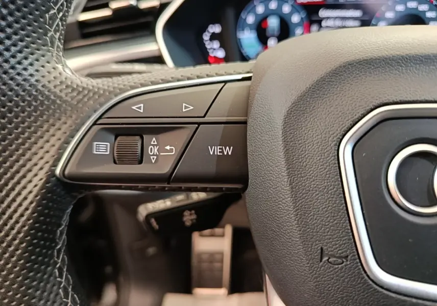 Gros plan sur le volant cuir noir perforé de l'Audi Q3 Sportback 2024 avec commandes multifonctions et affichage numérique flou.