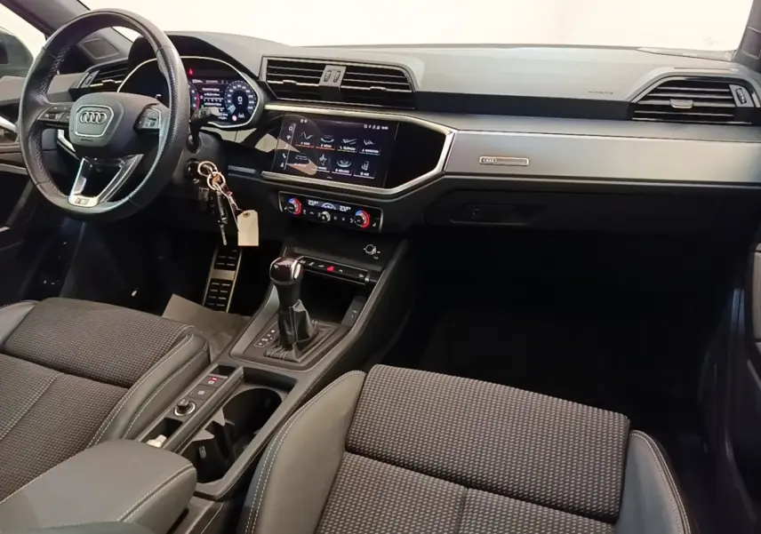 Vue intérieure de l’Audi Q3 Sportback 2024, tableau de bord et console centrale avec écran tactile et volant cuir noir.