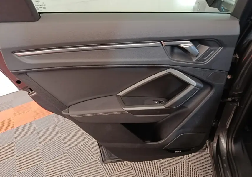 Vue intérieure de la porte avant gauche de l'Audi Q3 Sportback 2024, garniture noire avec insert argenté et haut-parleur Sonos.