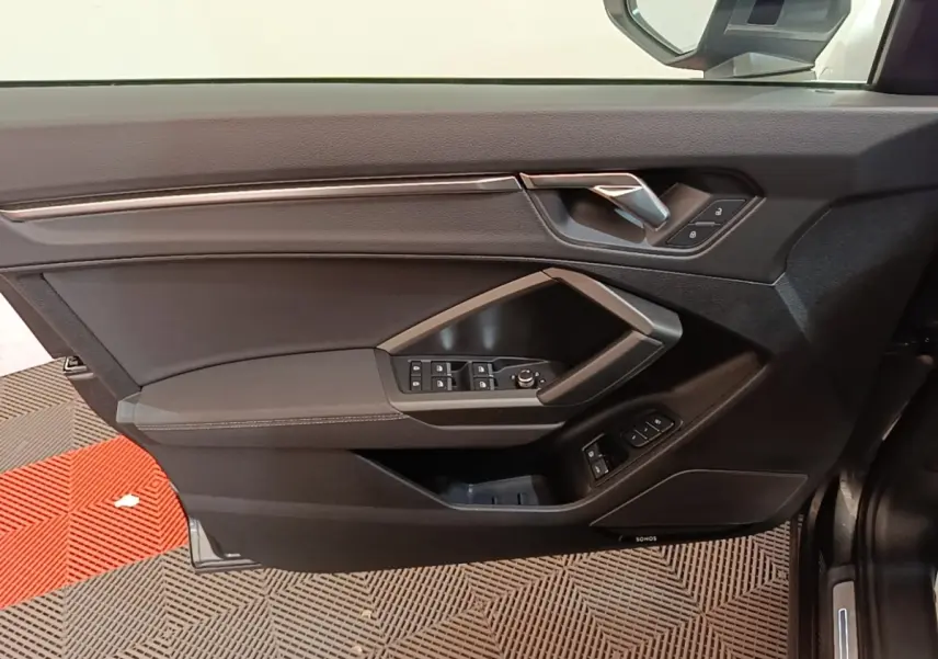 Vue intérieure sur la porte avant gauche noire de l'Audi Q3 Sportback 45 TFSI e 2024 avec commandes électriques et poignée métallique.