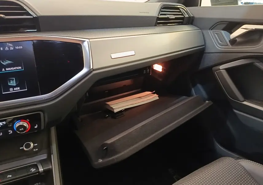 Intérieur de l'Audi Q3 Sportback 2024, vue côté passager sur la boîte à gants ouverte avec éclairage intérieur.