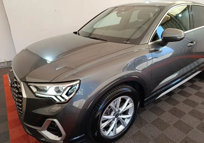 Audi Q3 Sportback gris clair en 3/4 avant droit, avec phares LED et jantes alliage visibles.
