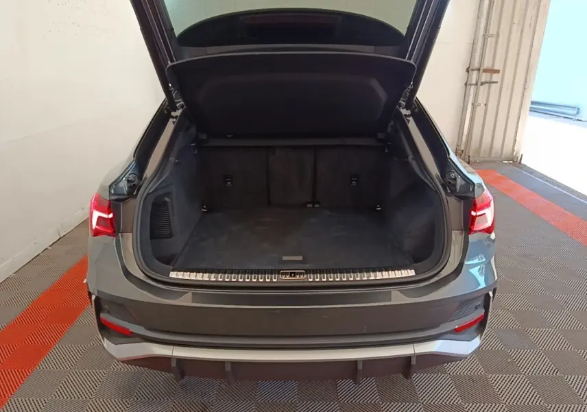 Vue arrière d'un Audi Q3 Sportback gris clair 2024 avec coffre ouvert montrant un espace de chargement vide.