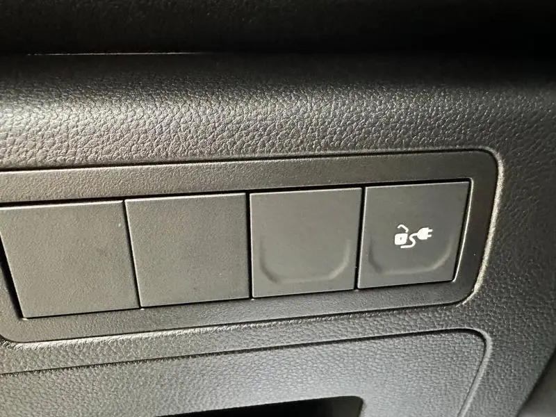 Bouton noir avec symbole de prise électrique sur le tableau de bord du Nissan Townstar L1 EV gris 2024.