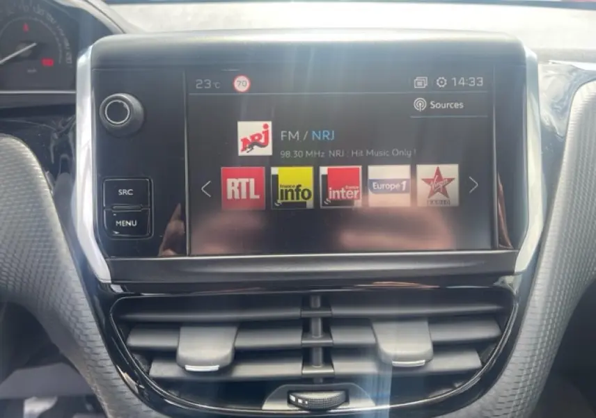 Écran tactile central de la Peugeot 208 blanc perle, affichant les stations radio FM avec commandes autour.