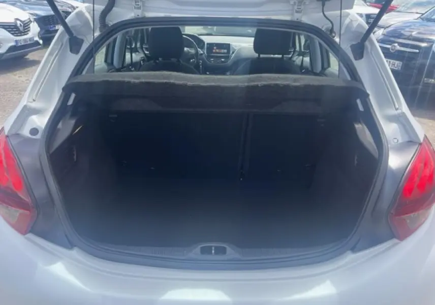 Vue arrière du coffre ouvert d'une Peugeot 208 blanc perle, montrant l'intérieur spacieux et la tablette cache-bagages.