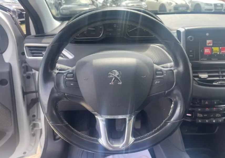 Vue rapprochée du volant cuir noir multifonction d'une Peugeot 208 blanche perle, tableau de bord et écran tactile visibles.