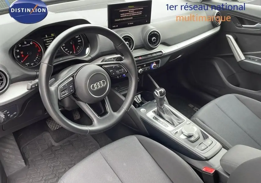 Intérieur noir de l'Audi Q2 35 TFSI 2023 vu côté conducteur, avec volant multifonction et console centrale moderne.