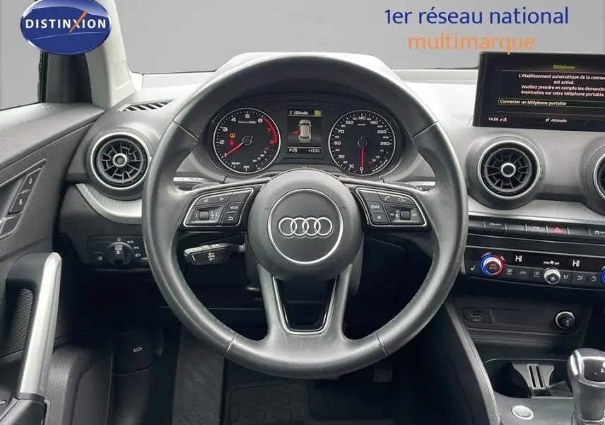Vue centrée sur le volant et le tableau de bord de l'Audi Q2 noir, avec écran multimédia et commandes au volant visibles.