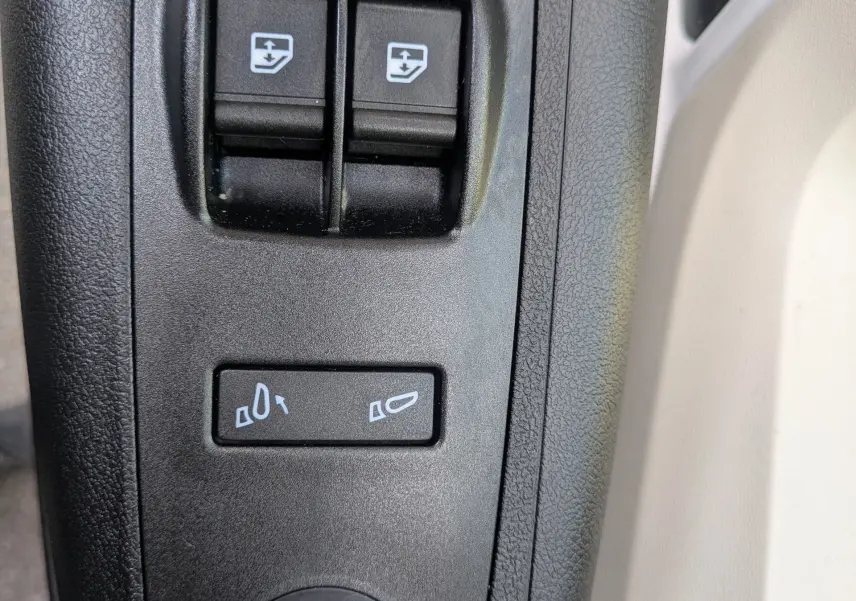 Gros plan sur les commandes de réglage des rétroviseurs noirs à gauche dans l'habitacle du Peugeot Boxer Fourgon blanc.