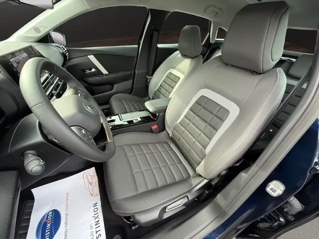 Vue intérieure côté conducteur de la Citroën C4 hybride bleue 2025, sièges avant en tissu et cuir gris avec tableau de bord moderne.