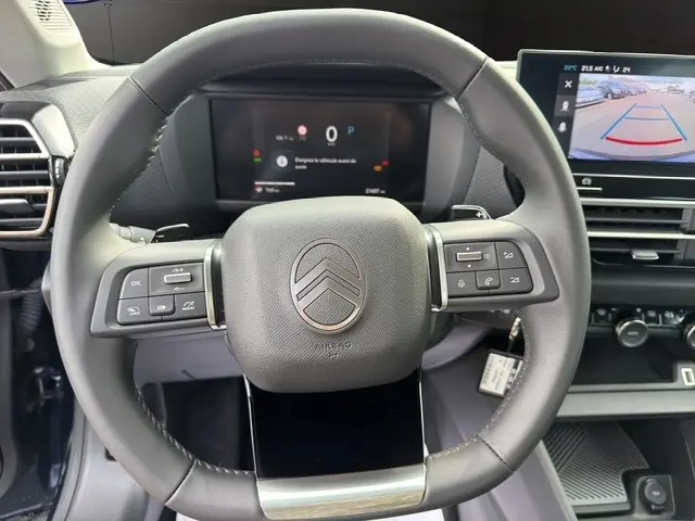 Vue intérieure centrée sur le volant cuir multifonctions de la Citroën C4 hybride 2025 avec écran de recul tactile visible.