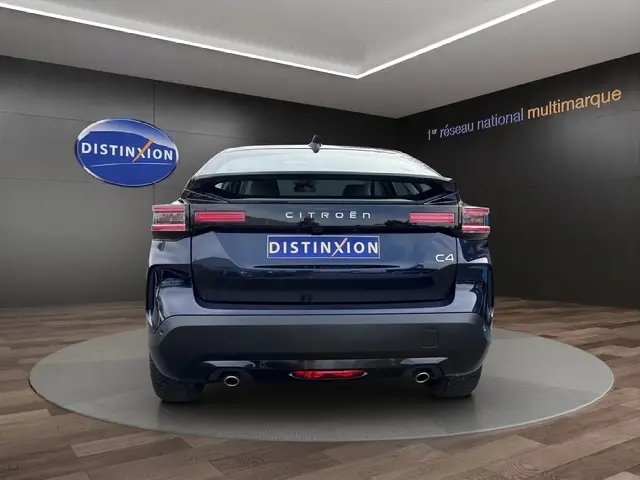 Vue arrière d'une Citroën C4 hybride bleu foncé avec feux LED et double sortie d'échappement en showroom.