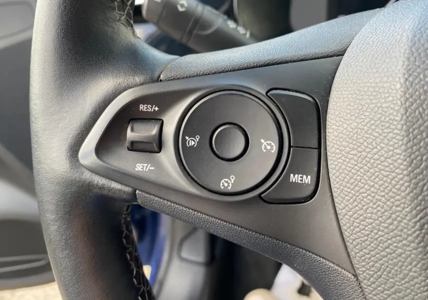 Gros plan sur les commandes du régulateur de vitesse au volant cuir de l'Opel Corsa bleu nautique 2021.