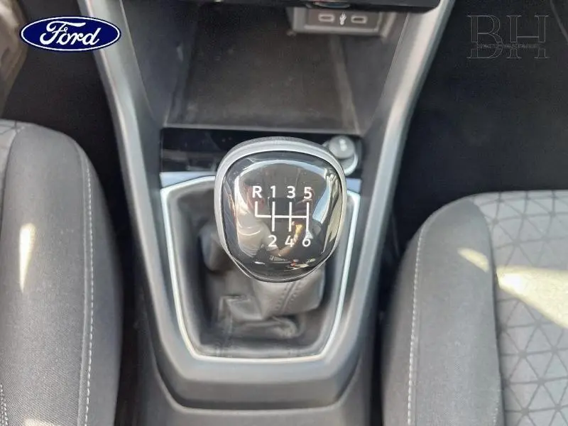 Le pommeau de levier de vitesse manuel noir vu de dessus entre deux sièges gris dans un intérieur de voiture.