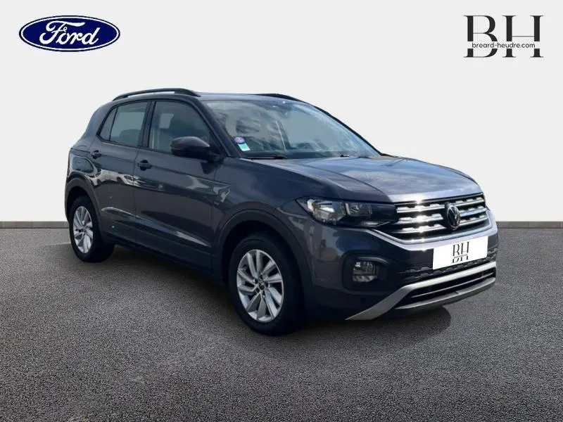 Volkswagen T-Cross gris cendré métallisé en 3/4 avant droit avec calandre chromée et barres de toit visibles.