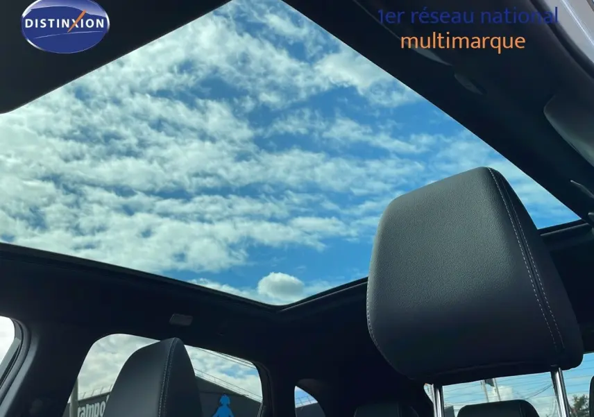 Vue intérieure du Nissan Qashqai 2025 blanc nacré avec toit noir, montrant le ciel à travers le toit panoramique et les appuis-tête cuir noir.