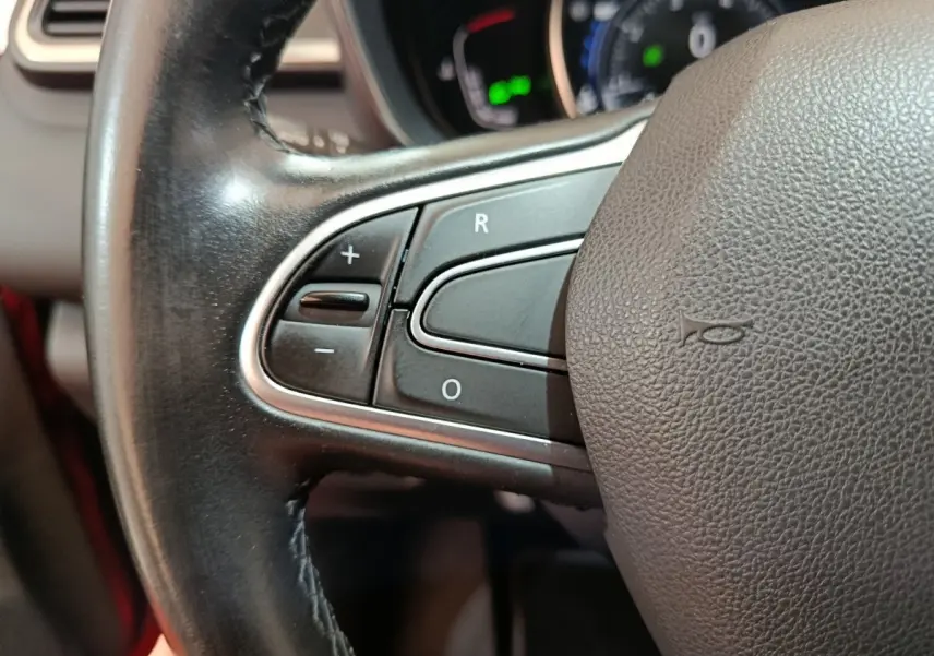 Gros plan sur les commandes de régulateur de vitesse au volant cuir du Renault Kadjar Intens rouge, tableau de bord flou en arrière-plan.