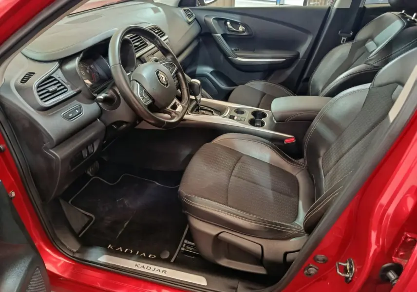 Vue intérieure côté conducteur du Renault Kadjar rouge, montrant le volant cuir multifonctions et les sièges noirs.