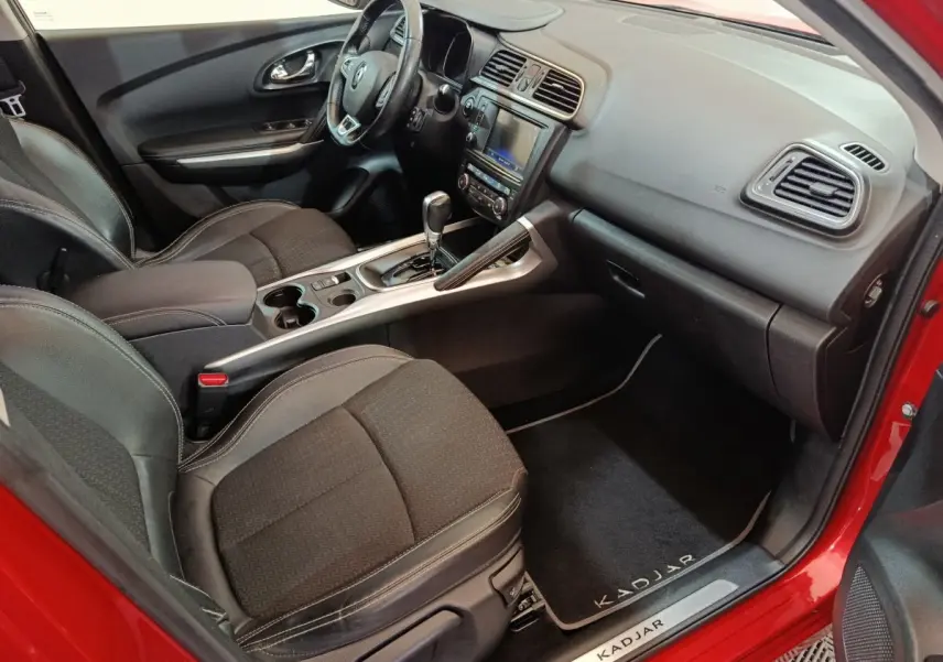 Intérieur côté passager du Renault Kadjar rouge, montrant sièges noirs et console centrale avec écran tactile.