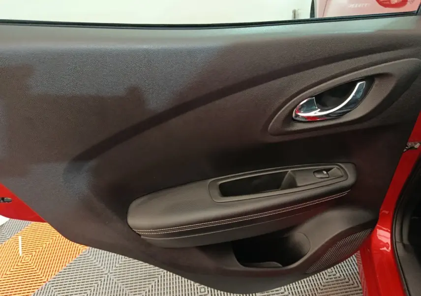 Gros plan sur la porte intérieure côté gauche du Renault Kadjar rouge, avec poignée chrome et accoudoir noir.